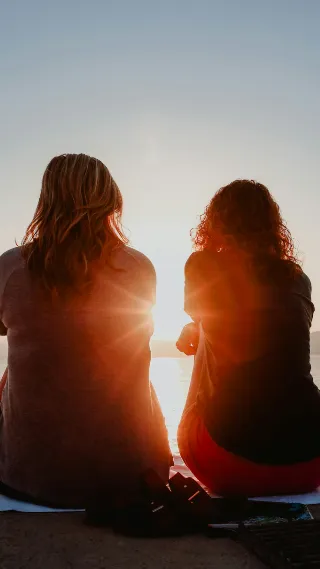 Two women silhoutted against sky and sun